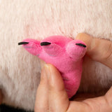 A close-up of a hand holding a small pink plush toy shaped like a pig's feet with black toenails, positioned against a soft white furry background.