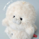 A fluffy cream-colored plush toy with large black eyes, a gray snout, and a small red tag at the bottom right, shown against a pale blue-gray background with white handwritten text overlay in the upper left.