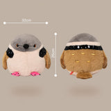 A plush bird toy shown from two angles on a plain beige background, with measurement lines indicating 32 cm width and 26 cm height. The toy has a gray and white head, black wing patches, pink feet, and a brown body with a black-and-white headband and small gold facial details.