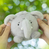 A small round gray plush elephant toy being held by two hands against a blurred green outdoor bokeh background.