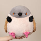 A cute, round, fluffy bird plush toy being held up by a person's hand against a plain beige background.