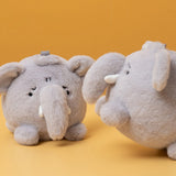 Two plush elephant toys in light gray fabric, one facing forward and one turned to the side, on a solid mustard yellow background.