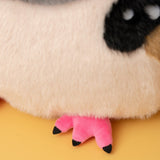 Close-up of a plush toy with cream-colored fur, a black patch around one eye, and bright pink feet with black tips, set against a solid yellow background.